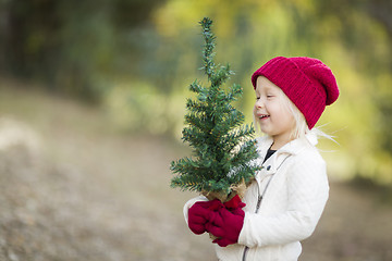 Image showing Baby Girl In Red Mittens and Cap Holding Small Christmas Tree