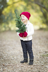 Image showing Baby Girl In Red Mittens and Cap Holding Small Christmas Tree