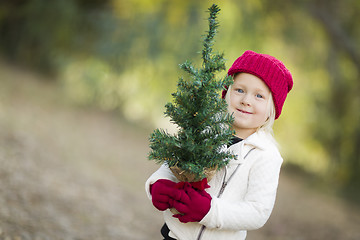 Image showing Baby Girl In Red Mittens and Cap Holding Small Christmas Tree