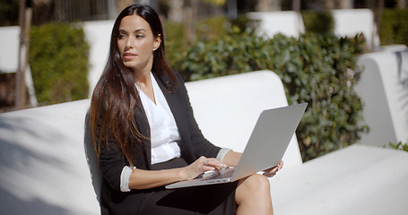 Image showing Young woman using a laptop on a white park bench