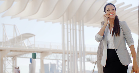 Image showing Gorgeous woman striding along chatting on a mobile