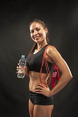 Image showing Muscular young woman athlete with a skipping rope on black 