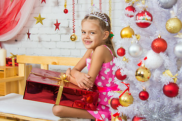 Image showing Smiling girl sitting on a bench with a huge gift from the Christmas trees