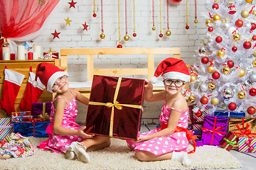 Image showing Two funny girl holding a great gift sitting on a rug