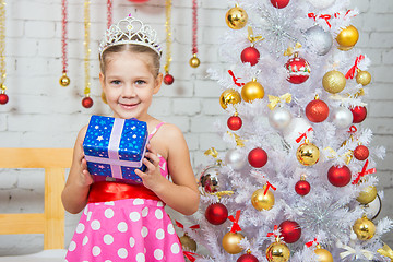 Image showing Happy little girl holding a Christmas gift and standing near Christmas trees