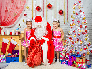 Image showing Santa Claus pulls out a bag of gifts to two girls