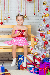 Image showing Girl sitting on a bench with a gift in his hand a snowy Christmas trees