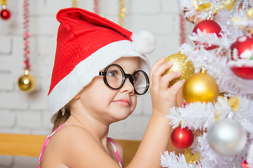 Image showing Girl with round glasses hangs balls on a snowy New Years Christmas tree