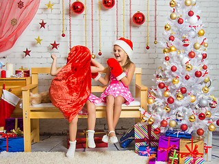 Image showing Girl in a cap and mittens of Santa Claus laughing at the girl who put a sack on his head