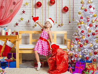 Image showing Girl in a cap and mittens of Santa Claus dancing around the bag with Christmas gifts