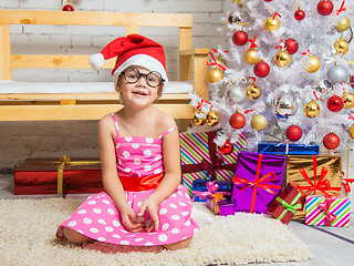 Image showing Girl in the red hat and the funny round glasses on a rug in a Christmas setting