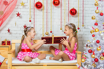 Image showing Girls sitting on a bench in a Christmas atmosphere and keep the big red gift in hands