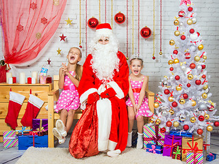 Image showing Happy girls and Santa Claus sitting on a bench in a Christmas setting