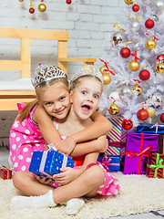 Image showing Girl hugging another girl sitting on a rug with a gift at Christmas tree