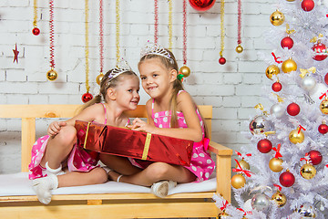 Image showing Girl whispering a secret that some other girl sitting on a bench with a Christmas present
