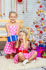 Image showing The girl gives a gift to his sister sitting on the rug in front of the Christmas tree