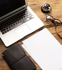 Image showing The laptop, blank paper, glasses and small bell on the wooden table 