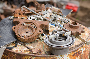 Image showing  A pile of old broken pieces of iron lying on a rusty barrel