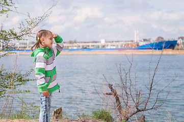 Image showing A girl stands near the river on which the floating ship and looks into the distance