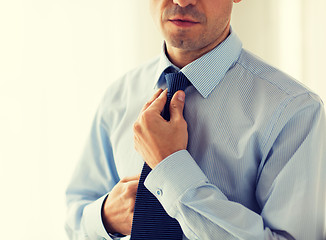 Image showing close up of man in shirt adjusting tie on neck