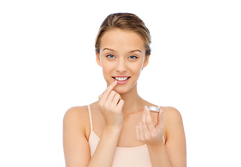 Image showing smiling young woman applying lip balm to her lips