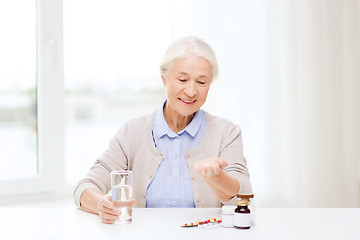 Image showing happy senior woman with water and medicine at home