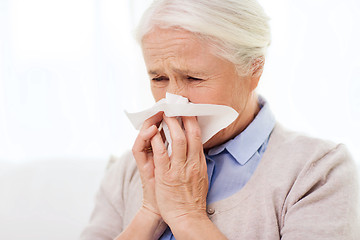 Image showing sick senior woman blowing nose to paper napkin