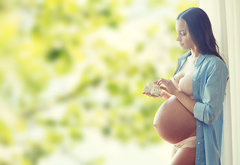 Image showing happy pregnant woman with baby booties at home