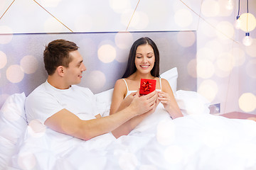 Image showing happy man giving woman little red gift box in bed