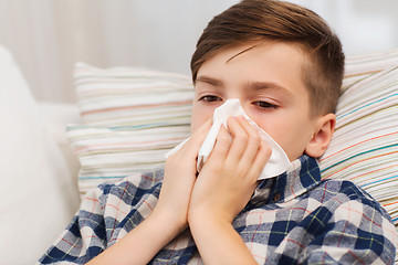 Image showing ill boy lying in bed and blowing his nose at home