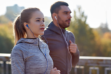 Image showing happy couple with earphones running in city