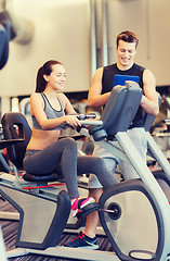 Image showing happy woman with trainer on exercise bike in gym