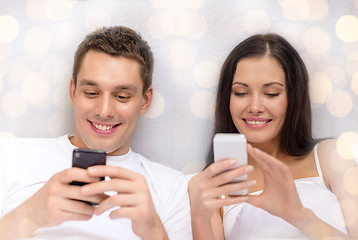 Image showing smiling couple in bed with smartphones