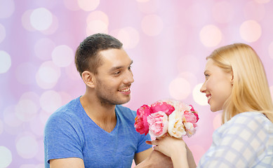 Image showing smiling man giving woman flowers at home