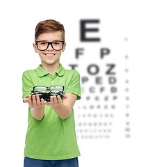 Image showing happy boy holding eyeglasses over eye chart