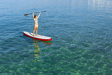 Image showing A beautiful and happy woman with arms up and learning paddle-sur