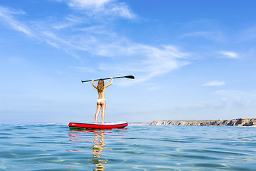 Image showing A beautiful and happy woman with arms up and learning paddle-sur