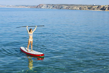 Image showing A beautiful and happy woman with arms up and learning paddle-sur