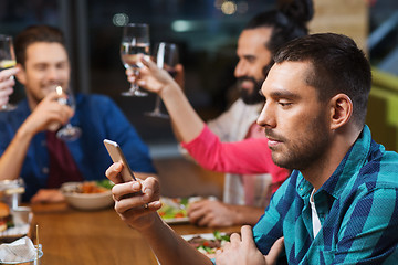 Image showing man with smartphone and friends at restaurant