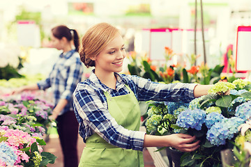 Image showing happy woman taking care of flowers in greenhouse