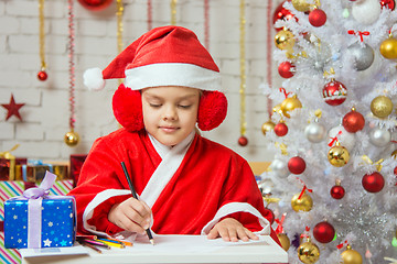 Image showing Girl dressed as Santa Claus writing on a sheet of paper sitting at the table