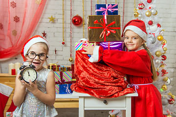 Image showing One girl keeps watch over time, 11-55, another in a suit of Santa Claus hugging a bag with gifts