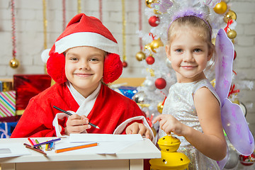 Image showing Girl dressed as Santa Claus writing a letter, standing next to a fairy with a flashlight in his hand