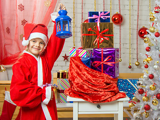 Image showing Girl dressed as Santa Claus stands with a candlestick in his hand a bag with Christmas gifts