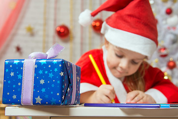 Image showing New Years gift in the foreground, in the background Girl draws pencil