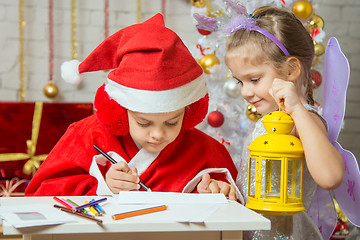 Image showing Girl dressed as Santa Claus signs the envelope with a letter, standing next to the fairy girl with a flashlight in his hand