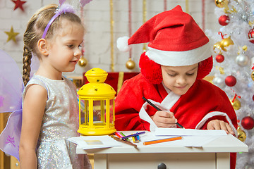 Image showing  Girl dressed as Santa Claus signs the envelope with a letter, standing next to a girl dressed as fairies