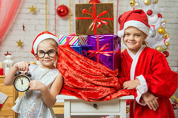 Image showing Girl shows on the clock, a girl dressed as Santa Claus is standing at the bag with gifts