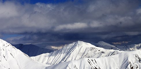 Image showing Panoramic view on snowy sunlit mountains and cloudy sky