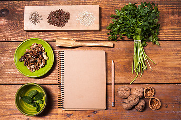 Image showing Notebook for recipes, walnuts, parsley and seeds on wooden table.